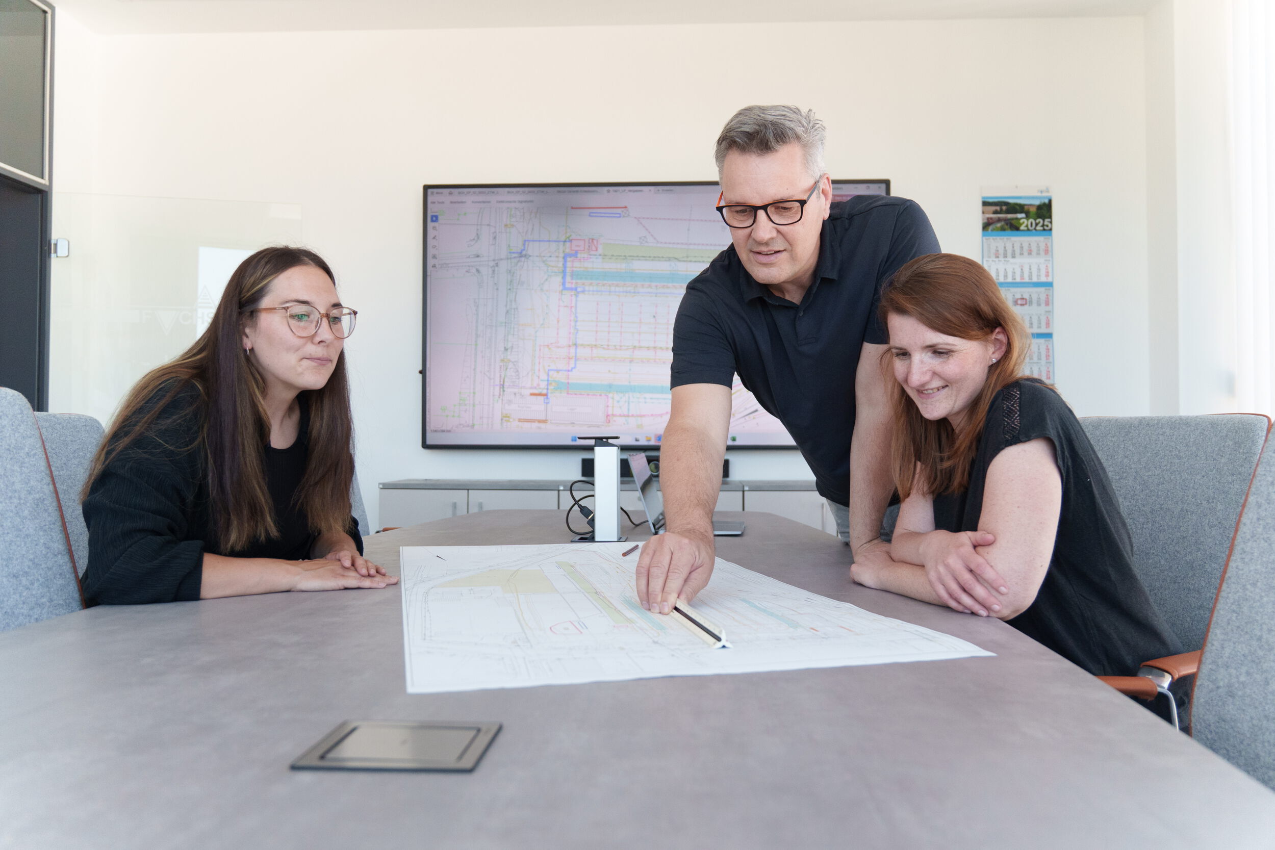 Fachgruppe schaut über einen Bauplan im Seminarraum
